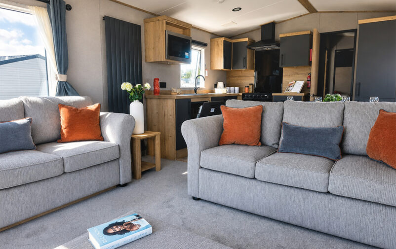 Modern living room with grey sofas and open-plan kitchen at Lovat Parks.