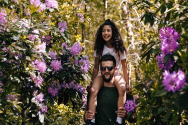 A dad with his daughter oh his shoulders in a forest.