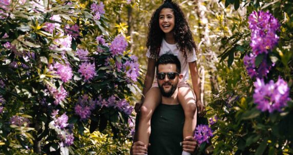 A dad with his daughter oh his shoulders in a forest.