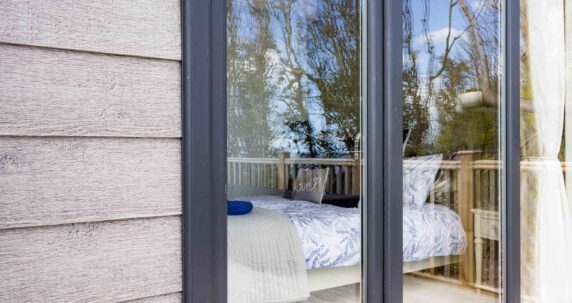 The outside of a lodge showing a bedroom through the glass.