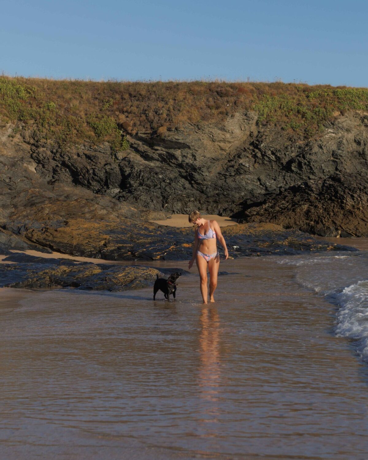 Woman walking down a beach with her dog.